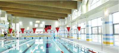Kryty basen sportowy z torami pływackimi, chorągiewkami i dużymi oknami