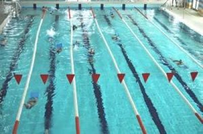 Pływacy trenują w basenie sportowym na wyznaczonych torach z czerwonymi chorągiewkami