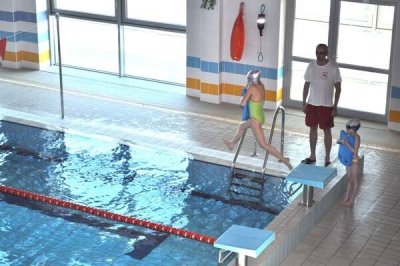 Dzieci z instruktorem na krytym basenie, jedna dziewczynka schodzi po drabince do wody