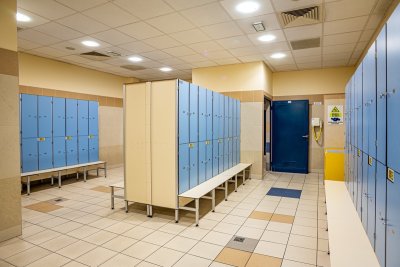 Szatnia z niebieskimi szafkami, ławkami i kabinami przebieralni w jasnym wnętrzu