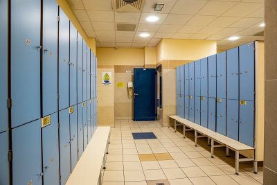 Szatnia z niebieskimi szafkami, ławkami i kafelkową podłogą w obiekcie sportowym