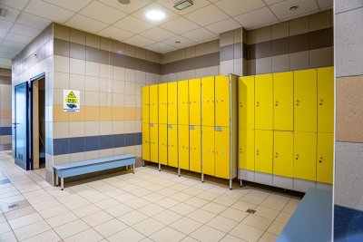 Szatnia basenowa z żółtymi szafkami, ławkami i tabliczką ostrzegającą przed śliską podłogą