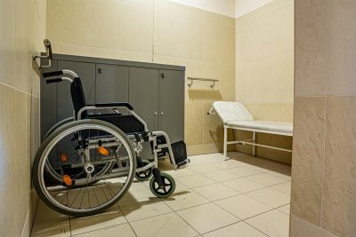 Wózek inwalidzki w łazience dostosowanej dla osób z niepełnosprawnościami, obok leżanka i uchwyty