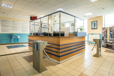 Recepcja z ladą, bramkami wejściowymi i automatami w jasnym holu budynku