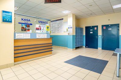 Hol basenu z kasą, szafkami i wejściami do toalet wewnątrz obiektu sportowego