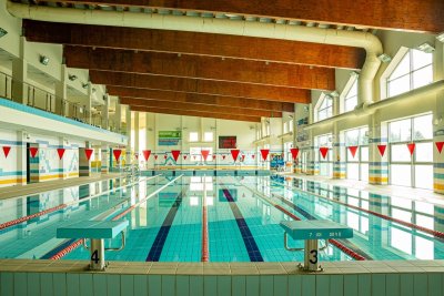 Kryty basen sportowy z torami pływackimi, słupkami startowymi i drewnianymi belkami stropowymi