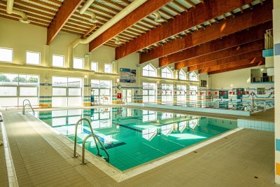 Kryty basen z torami pływackimi, dużymi oknami i drewnianymi belkami stropowymi