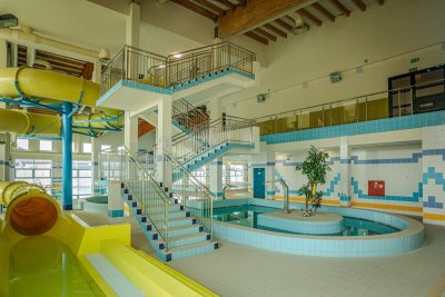 Wnętrze aquaparku z żółtymi zjeżdżalniami, schodami i płytkim basenem z wyspą pośrodku