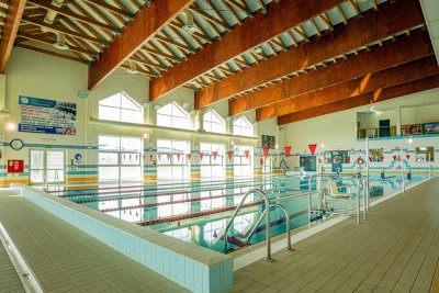 Kryty basen sportowy z torami pływackimi, dużymi oknami i drewnianymi belkami stropowymi