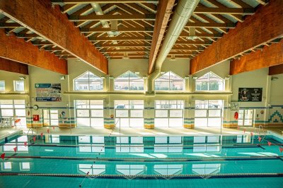 Kryty basen sportowy z torami pływackimi, dużymi oknami i drewnianą konstrukcją dachu