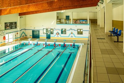 Kryty basen sportowy z torami pływackimi, trybunami i drewnianym sufitem w jasnej hali