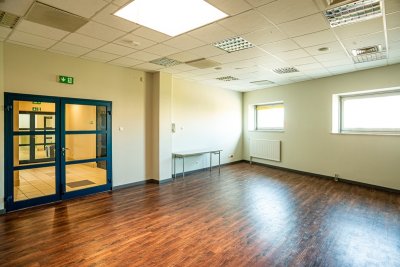 Puste pomieszczenie biurowe z drewnianą podłogą, przeszklonymi drzwiami, oknami i oświetleniem sufitowym