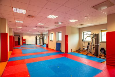 Sala treningowa ze sprzętem do ćwiczeń, matami na podłodze i workami bokserskimi