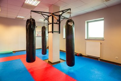 Sala treningowa z workami bokserskimi zawieszonymi na stelażu i matami na podłodze