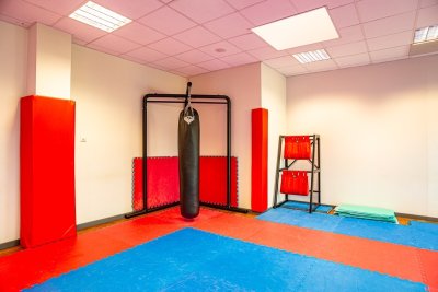 Sala treningowa z workiem bokserskim, matami i ochraniaczami na ścianach