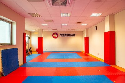 Sala treningowa karate z czerwono-niebieskimi matami i osłonami na ścianach