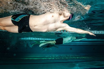 Pływak pod wodą płynie kraulem w basenie sportowym, obok torów pływackich