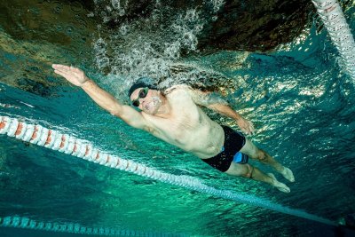 Mężczyzna pływa kraulem pod wodą w basenie sportowym między torami pływackimi