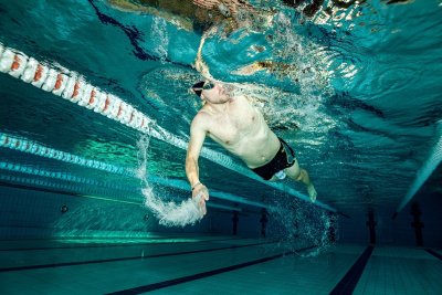 Pływak w okularach płynie pod wodą kraulem w basenie sportowym obok torów pływackich