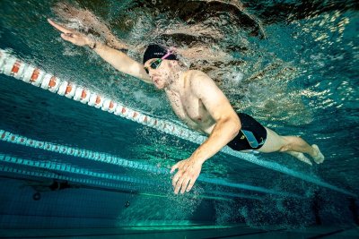 Pływak w okularach i czepku płynie kraulem pod wodą w basenie sportowym