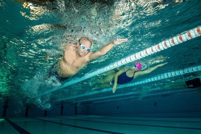 Pływacy w okularach i czepku trenują kraulem pod wodą na torach basenu sportowego