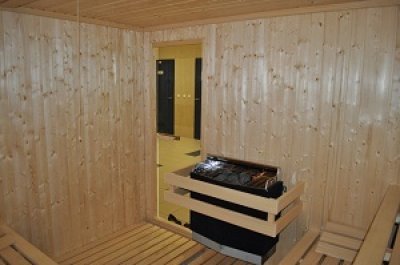 Drewniana sauna z piecem i otwartymi drzwiami do jasnego pomieszczenia
