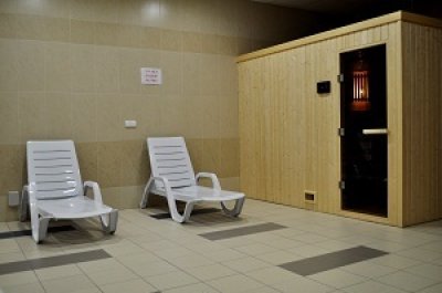 Dwa białe leżaki w strefie relaksu przy drewnianej saunie w pomieszczeniu wellness